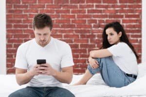 Couple struggling with trust issues — man focused on phone while woman looks upset, symbolizing infidelity and emotional disconnection.
