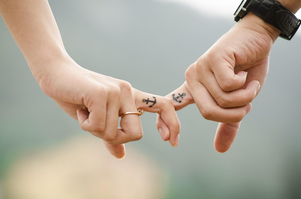 Close-up of couple holding fingers with matching anchor tattoos, symbolizing trust and deep emotional connection.