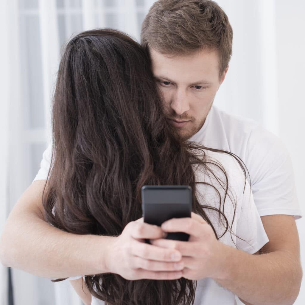A man hugs his partner while secretly looking at his phone representing micro-cheating and emotional infidelity in relationships.